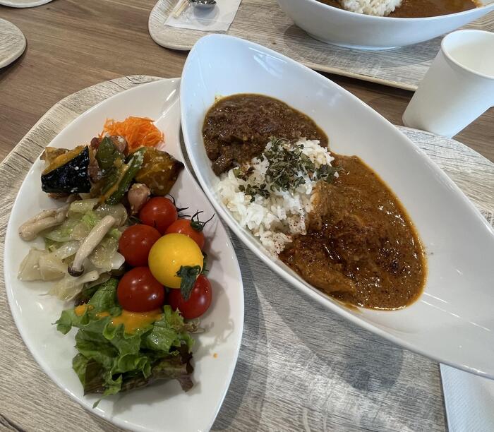 レストランが提供するサラダ類を自分で一つの器に盛り付け、もう一つの器にご飯と2種類のカレーをかけて仕上げます