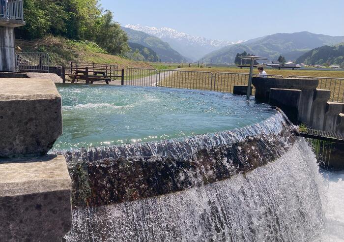 東山円筒分水槽を囲む水の流れと田園風景、毛勝三山の山並みが重なる絶