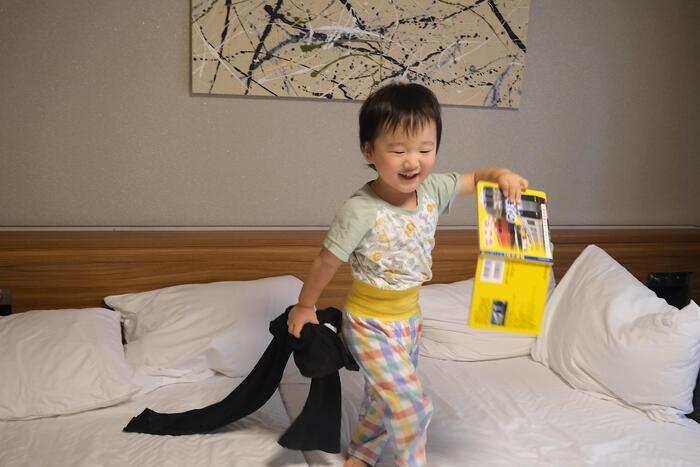 子供がベットの上で絵本を片手に笑顔の様子