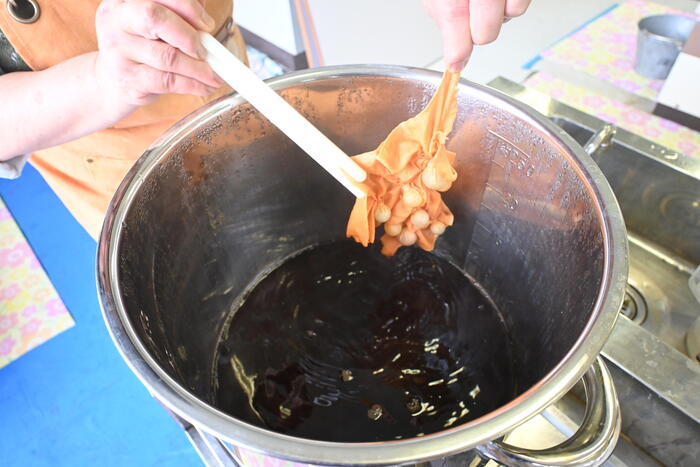 鍋にりんごの枝葉を煮出してつくった染液に布を浸けている