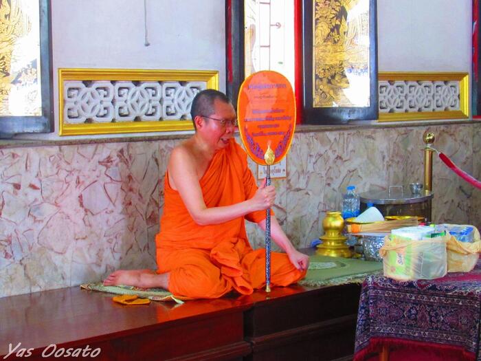 タイの寺院本堂に安置された黄金に輝く大きな仏像と正座で祈る僧侶